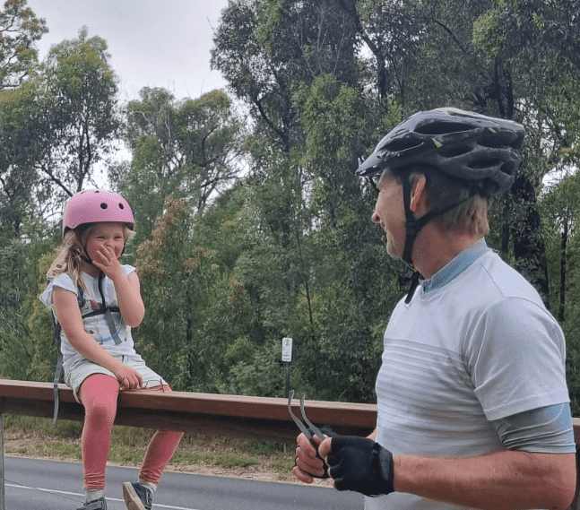 jono farrington in bike gear with daughter sitting on fence